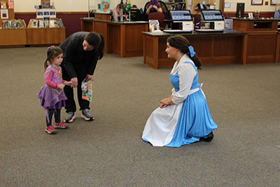 Costumed princess kneels down to greet a child (in costume) and adult.