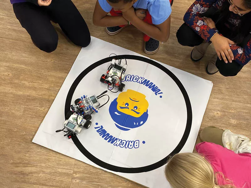 Looking down at children encircling a couple of robots battling.